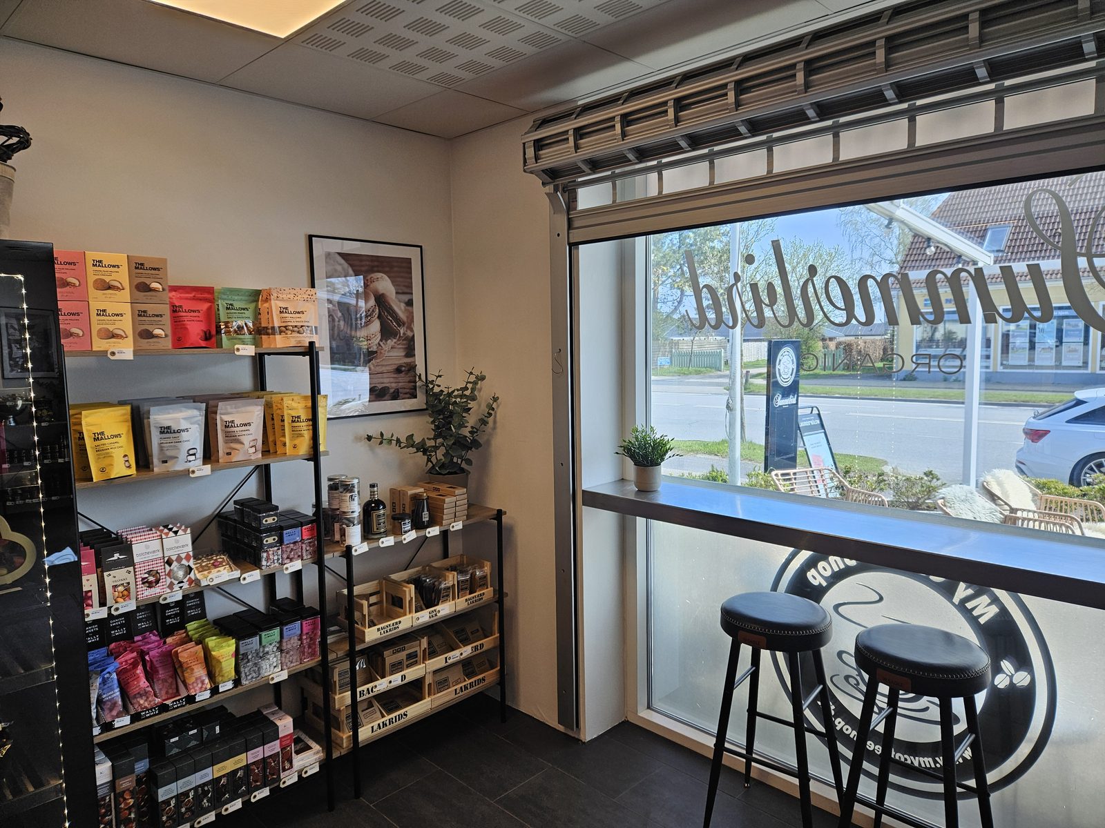 Inde i My Coffee Shop i Greve Strand — hylder med chokolade og delikatesser ved vinduet